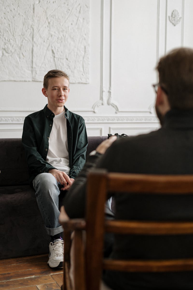 Man in Black Sweater Sitting on Brown Wooden Chair